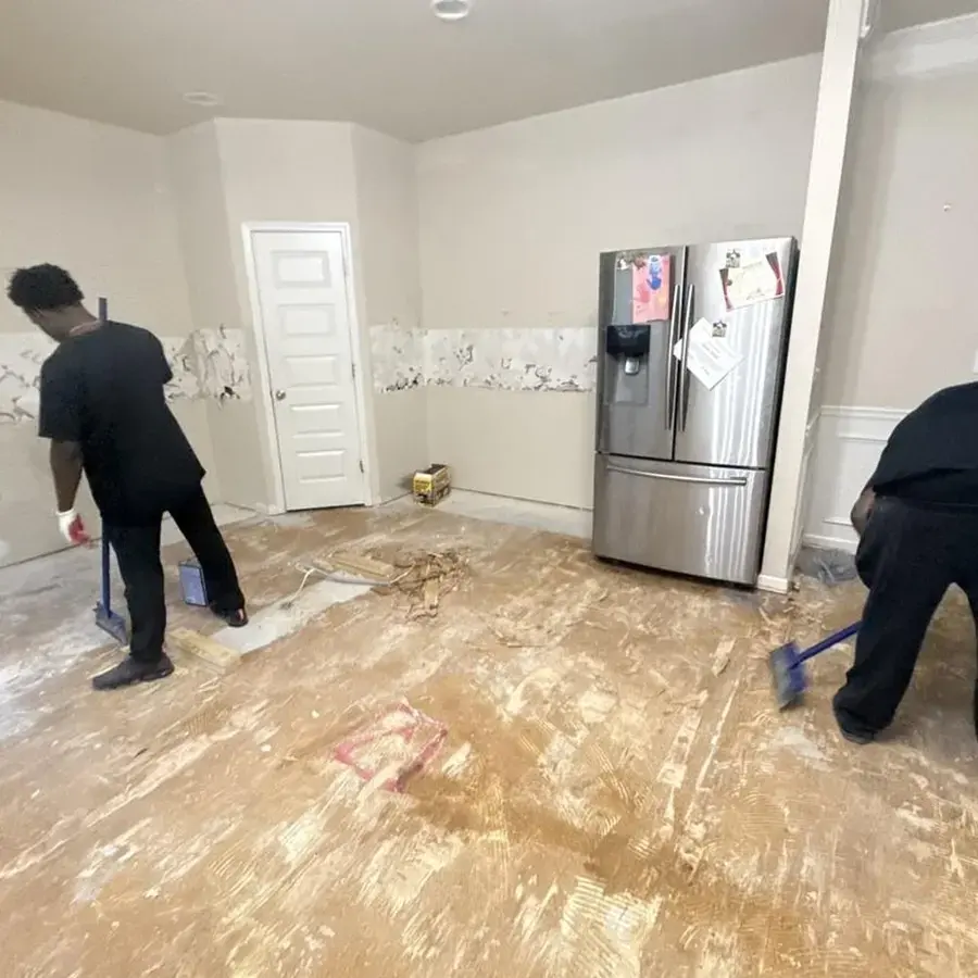 Technicians cleaning a wet kitchen subfloor after an appliance leak beside the refrigerator
