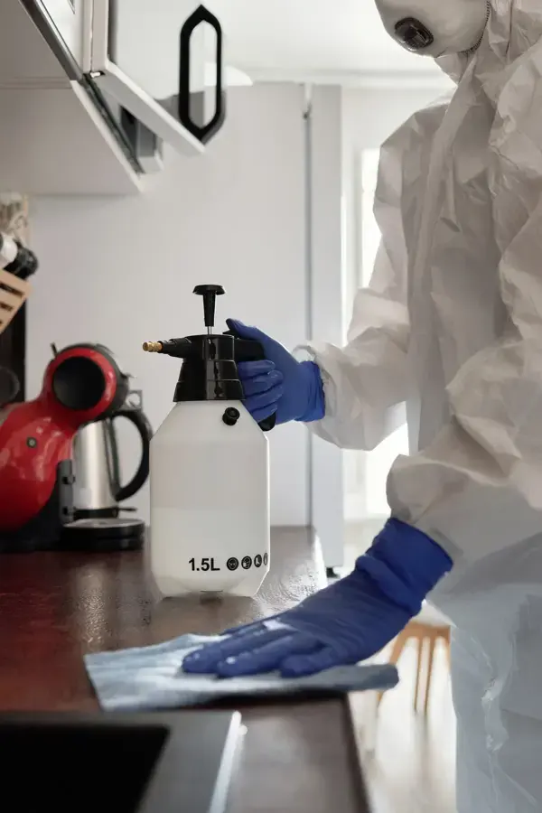 Gloved technician in a protective suit applying antimicrobial to a counter after a sewage backup