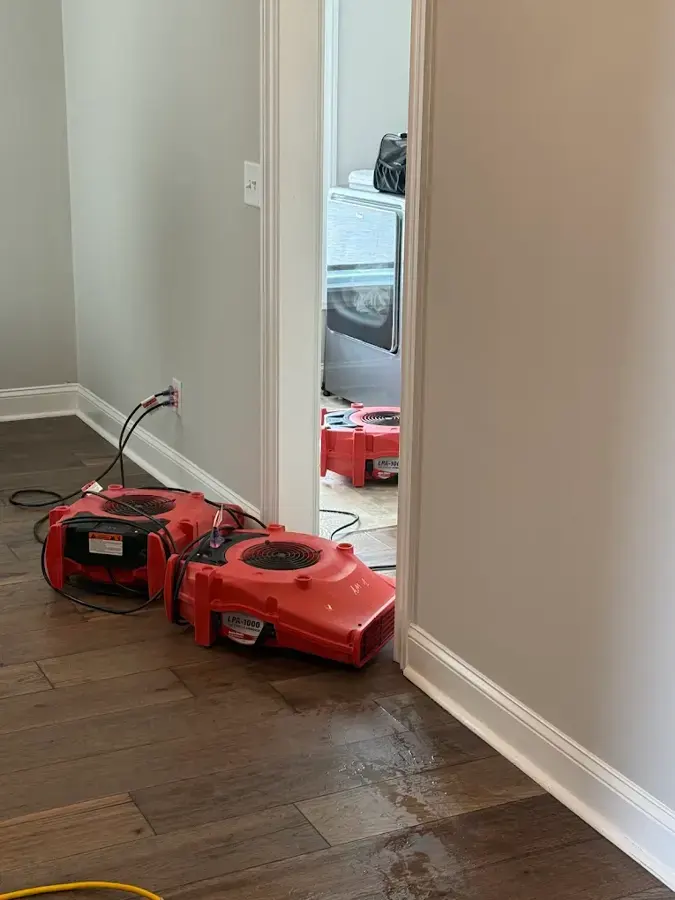Two red air movers drying hardwood flooring and the base of a wall