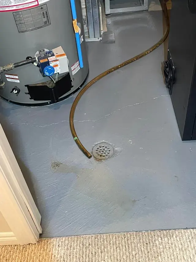 Gas water heater with water spread across the utility room floor toward the drain